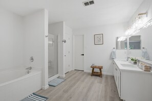 A modern bathroom with a bathtub, a shower, a vanity with a mirror, and a small stool. - New Luxury & Spacious 5BR/3BA Retreat–Sleeps 16 – Prime location & Fully Stocked (McKinney)