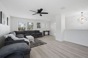 A modern living room with a sectional sofa, a small table, a ceiling fan, and a geometric pendant light. - New Luxury & Spacious 5BR/3BA Retreat–Sleeps 16 – Prime location & Fully Stocked (McKinney)