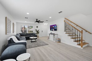 A modern living room with a grey sectional sofa, a coffee table, and a TV mounted on the wall. - New Luxury & Spacious 5BR/3BA Retreat–Sleeps 16 – Prime location & Fully Stocked (McKinney)