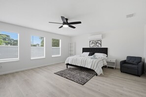 A bedroom with a bed, a ceiling fan, a nightstand, a chair, and a window with blinds. - New Luxury & Spacious 5BR/3BA Retreat–Sleeps 16 – Prime location & Fully Stocked (McKinney)