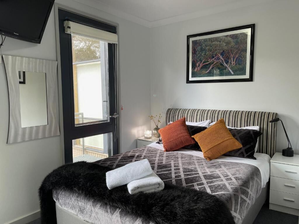 A bedroom with a bed, a nightstand, a lamp, a painting, and a window.