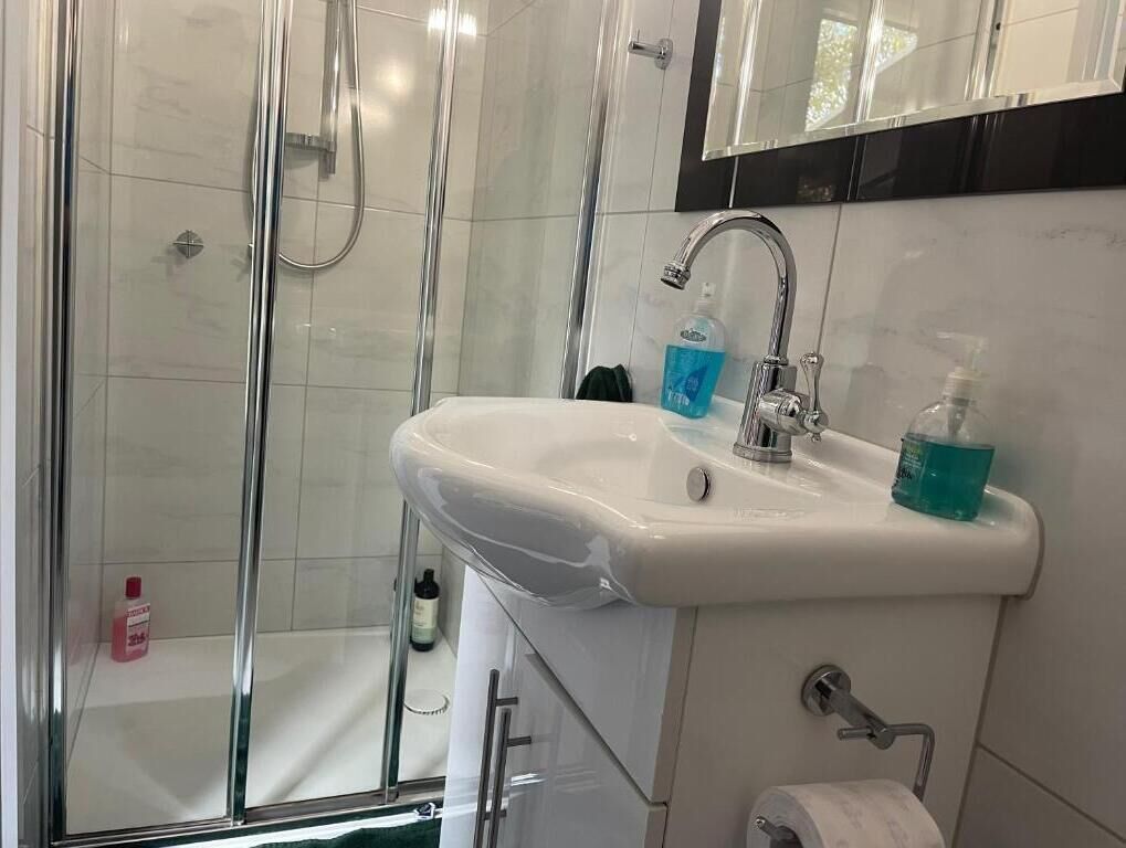 A bathroom with a glass-enclosed shower, a white sink with a mirror above it, and toiletries on the sink.