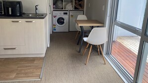 Ett kompakt kök med en kaffebryggare, en tvättmaskin och en matplats med stolar.