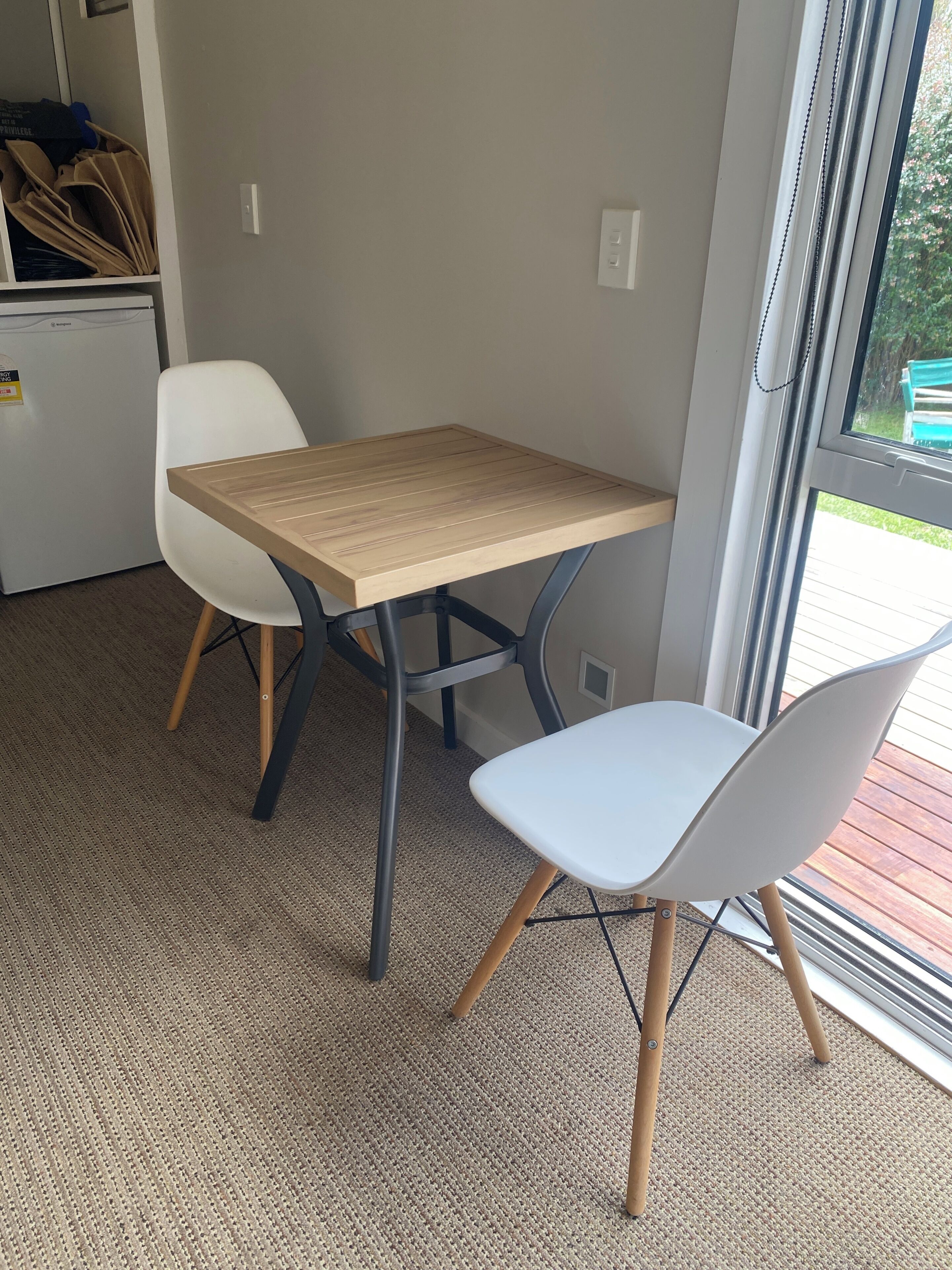 Une pièce avec une petite table et deux chaises, un sol recouvert de moquette et une fenêtre donnant sur un paysage verdoyant.