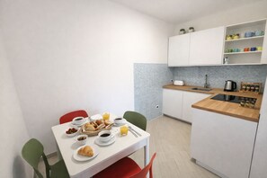 A small kitchenette with a sink, a stove, and a countertop. There is a dining table with chairs and a breakfast spread. - Lungomare del Cavo  Sea Just Steps Away (Rio Marina)