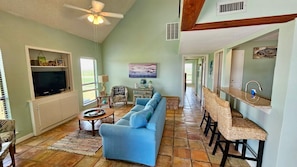 A living room with a sofa, TV, and a dining area with chairs. - Condo in the Dunes w/beach at a glance, & pool (Matagorda)