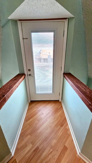 A narrow hallway with wooden flooring, a white door with a window, and wooden trim on the walls. - Condo in the Dunes w/beach at a glance, & pool (Matagorda)