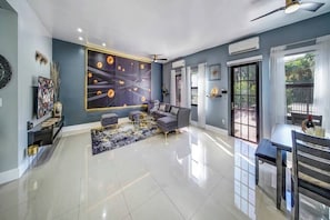 A modern living room with a large abstract painting, a sofa, a coffee table, and a dining area with a table and chairs. - Glamorous 2Bed/2Bath/2K- 5★ DT Location-♛Hot Tub (Fort Lauderdale)