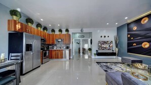 A modern kitchen with wooden cabinets, a stainless steel refrigerator, and a dining area with a table and chairs. - Glamorous 2Bed/2Bath/2K- 5★ DT Location-♛Hot Tub (Fort Lauderdale)