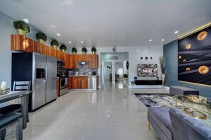 A modern kitchen with wooden cabinets, a stainless steel refrigerator, and a dining area with a table and chairs. - Glamorous 2Bed/2Bath/2K- 5★ DT Location-♛Hot Tub (Fort Lauderdale)