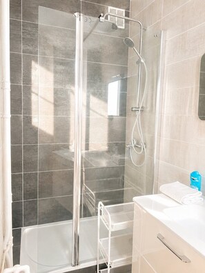 A shower with a glass door, a white sink, and a towel rack. - Le Valéry - Calme sur cour -Paris 16 (Paris)