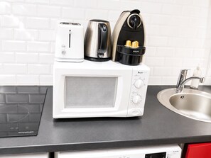 A kitchen with a white microwave, a toaster, a kettle, and a coffee maker on the counter. - Le Valéry - Calme sur cour -Paris 16 (Paris)