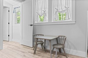 A room with a table and two chairs, a door, and a window with curtains. - Toddy View - NEW! Waterfront Home on Toddy Pond (Blue Hill)