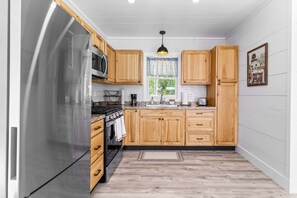 A kitchen with wooden cabinets, a stainless steel refrigerator, a microwave, a stove, and a window with a view. - Toddy View - NEW! Waterfront Home on Toddy Pond (Blue Hill)