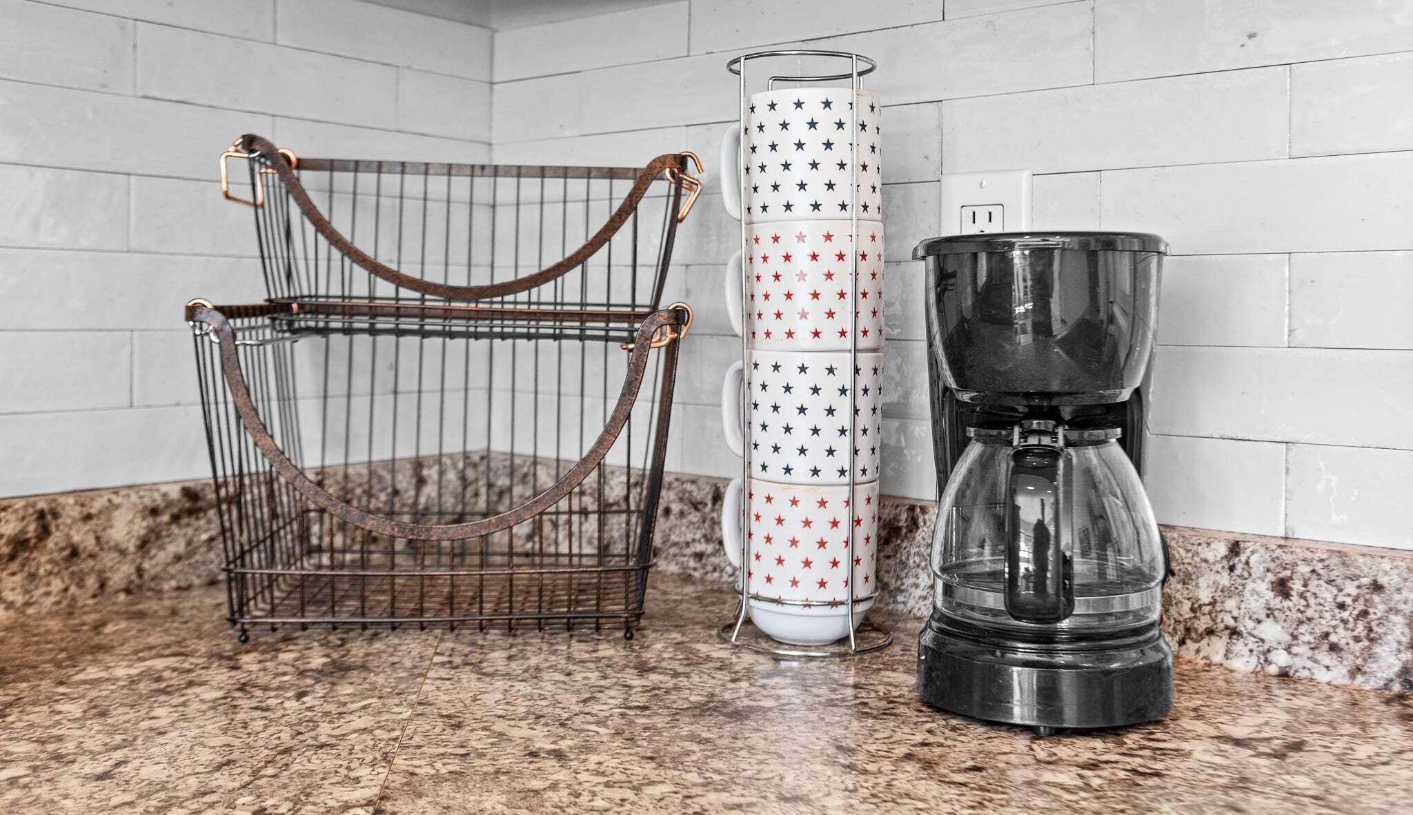 A kitchen counter with a coffee maker, a metal basket, and a tall glass container.