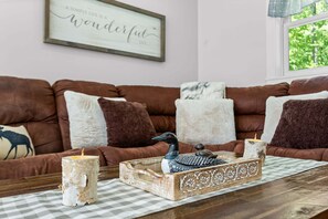 A cozy living room with a brown leather sofa, decorative pillows, a wooden tray with a bird figurine, a candle, and a framed inspirational quote on the wall. - Toddy View - NEW! Waterfront Home on Toddy Pond (Blue Hill)