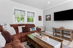 A living room with a brown leather sofa, a wooden coffee table, and a flat-screen TV mounted on the wall. - Toddy View - NEW! Waterfront Home on Toddy Pond (Blue Hill)