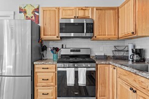 A kitchen with wooden cabinets, a stainless steel refrigerator, a microwave, a stove, and a sink. - Toddy View - NEW! Waterfront Home on Toddy Pond (Blue Hill)