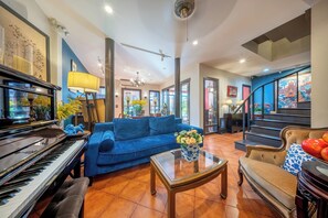 A spacious living area with a grand piano, a blue sofa, a glass coffee table, and a staircase leading to an upper level. - Aphirom Hometel (Bangkok)