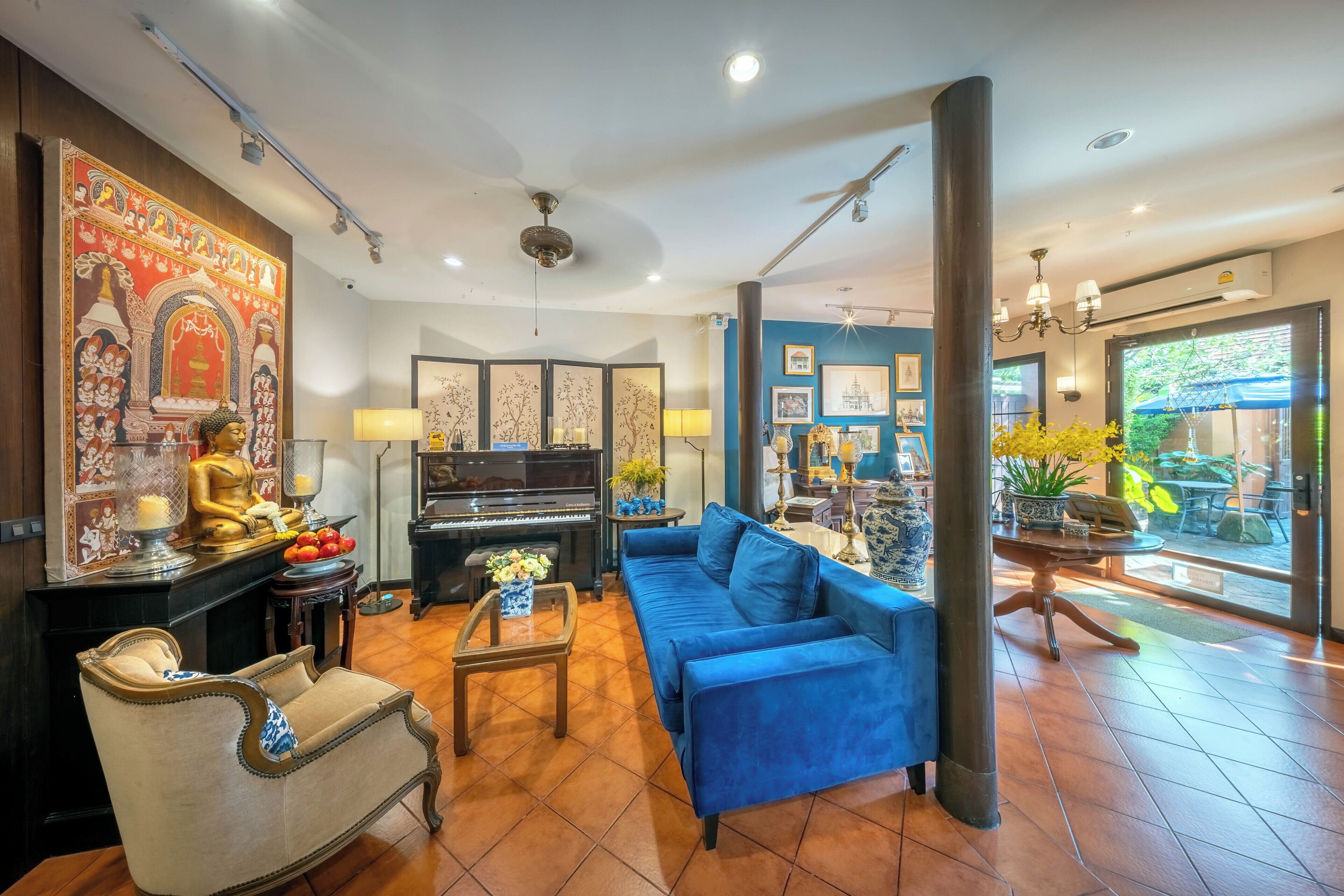 A living room with a blue sofa, a piano, a Buddha statue, and a decorative wall.