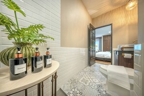 A bathroom with a white tiled wall, a large potted plant, three bottles of shampoo and conditioner, a toilet, and a mirror. - Aphirom Hometel (Bangkok)