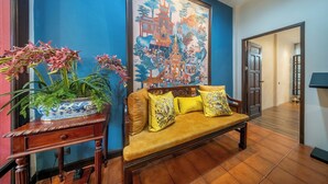 A room with a blue wall, a large painting, a sofa with yellow cushions, and a potted plant. - Aphirom Hometel (Bangkok)