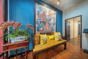 A room with a blue wall, a large painting, a sofa with yellow cushions, and a potted plant. - Aphirom Hometel (Bangkok)