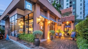 A modern hotel with a prominent sign, a brick-paved entrance, and surrounding greenery. - Aphirom Hometel (Bangkok)