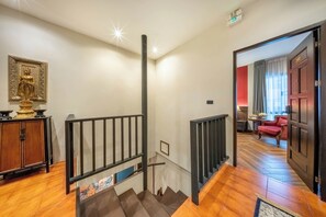 A staircase with a metal railing, a wooden cabinet with a golden statue, and a red door leading to a room with a red chair and a table. - Aphirom Hometel (Bangkok)
