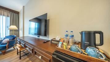 Ein Hotelzimmer mit einem Holztisch, einem Fernseher, einer Minibar, einer Kaffeemaschine und einem blauen Sessel.