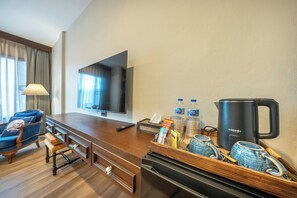 A hotel room with a wooden desk, a television, a minibar, a coffee maker, and a blue chair. - Aphirom Hometel (Bangkok)