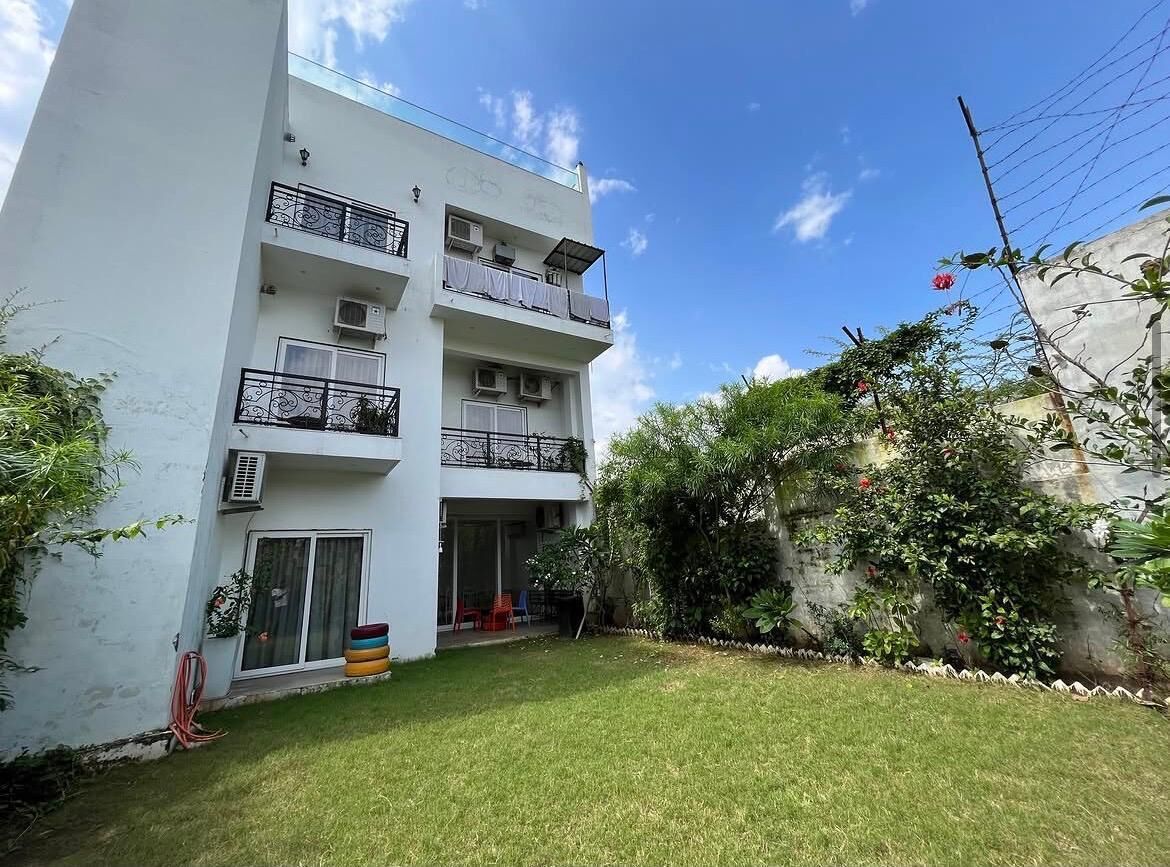 A multi-story building with balconies, a grassy yard, and a clear sky.