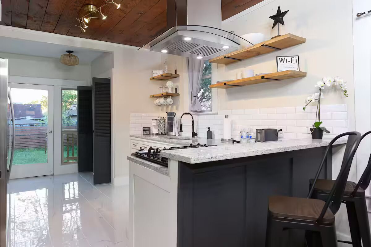 A modern kitchen with a central island, built-in appliances, and wooden shelves.