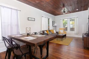 Un comedor con una mesa de madera dispuesta para cuatro, un sofá con cojines y un ventilador de techo.