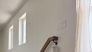 A wooden staircase with a handrail, a light switch, and a window.
