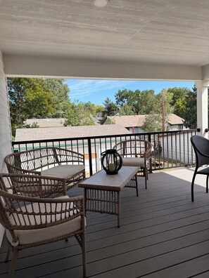 A covered outdoor seating area with wicker furniture and a table, overlooking a residential neighborhood.