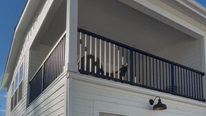 A two-story house with a garage, a balcony with a black railing, and a light fixture above the garage door.
