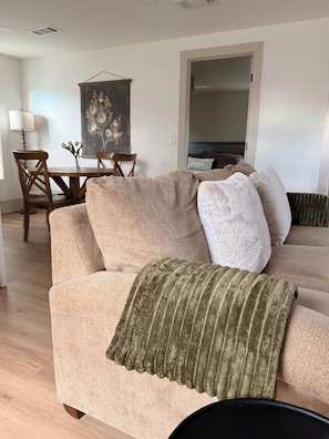 A beige sofa with a textured throw blanket, a dining table with chairs, and a painting on the wall.