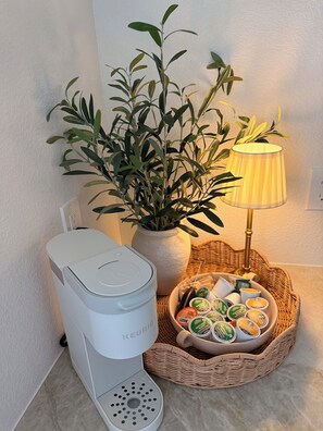 A Keurig coffee maker, a potted plant, a lamp, and a basket of coffee pods.