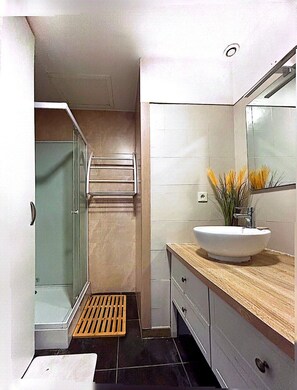 Un baño con cabina de ducha de vidrio, un lavabo blanco con encimera de madera y un espejo sobre el lavabo.