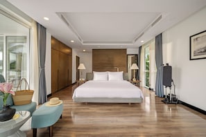 Ein modernes Hotelzimmer mit einem großen Bett, einer Sitzecke mit Sessel und Tisch, einer Stehlampe und einem großen Fenster mit Vorhängen.