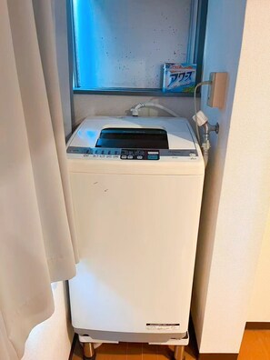 A compact, white, portable washing machine with a digital control panel, placed in a corner with a window above it. - Youki Residence (Suginami-ku)