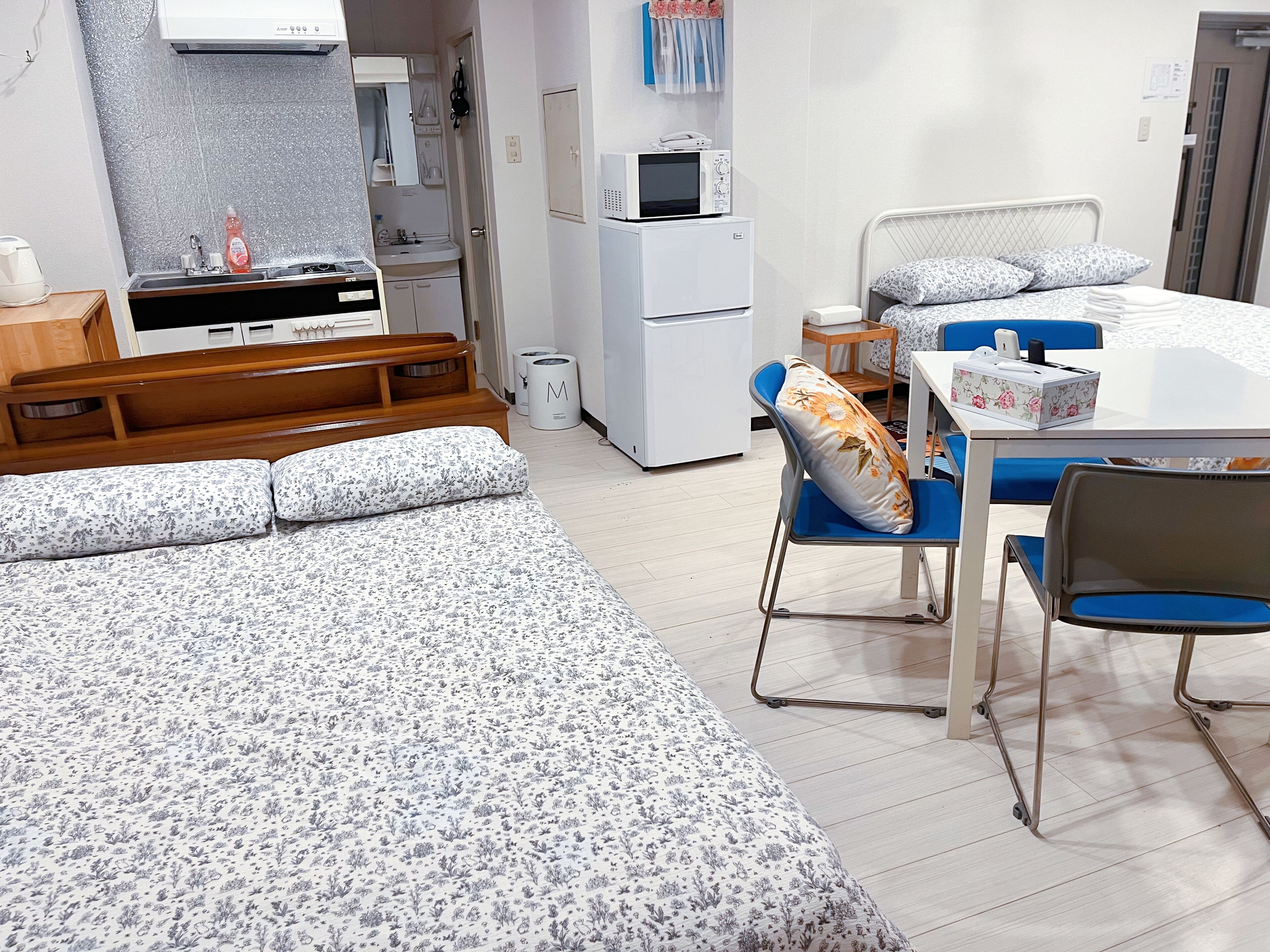 A hotel room with a bed, a desk, a chair, a microwave, a refrigerator, and a sink.