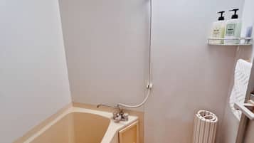 A bathroom with a bathtub, a shower, and a toilet. There are toiletries on a shelf.