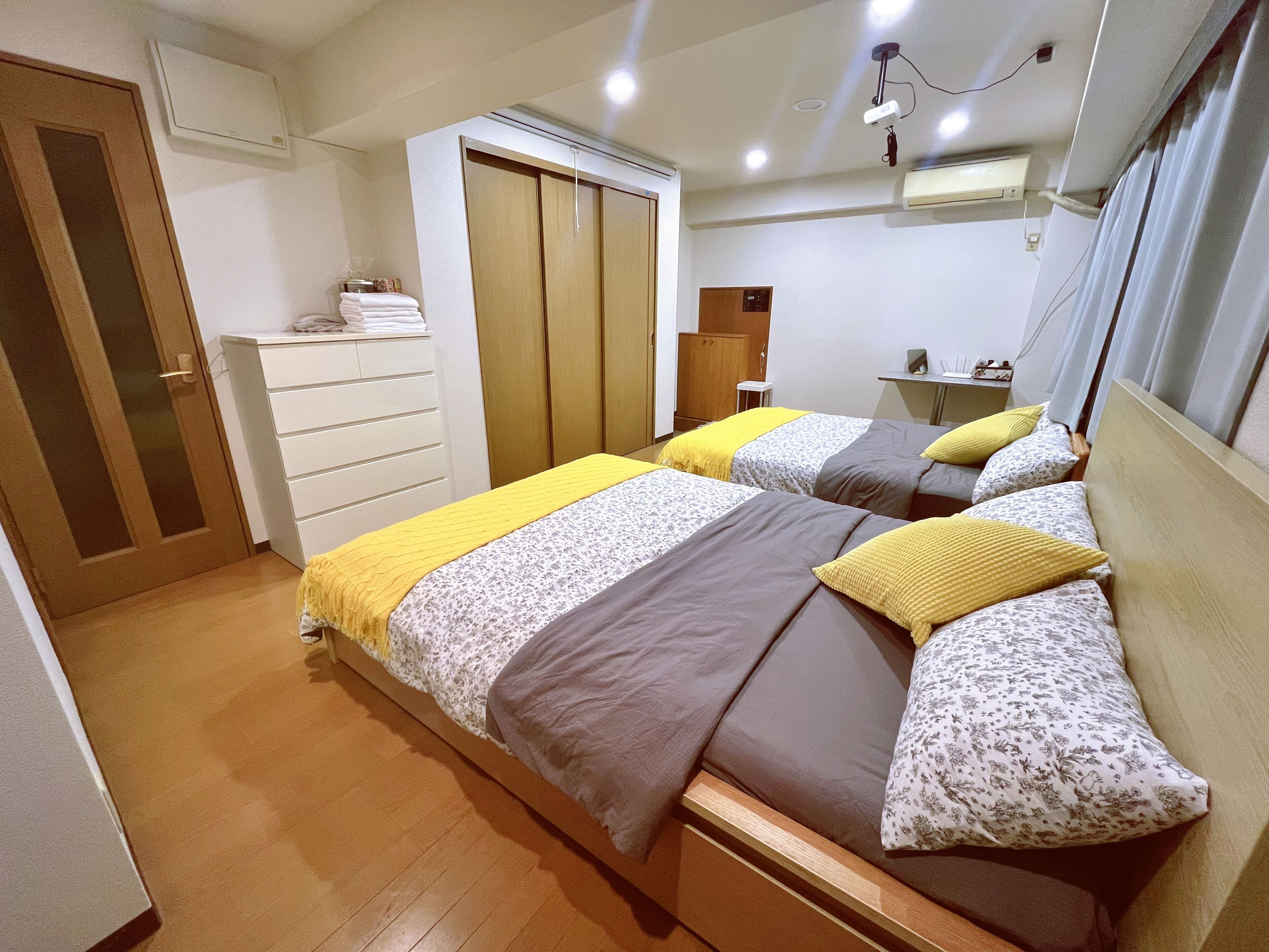 A bedroom with two beds, a wardrobe, a desk, and a mirror.