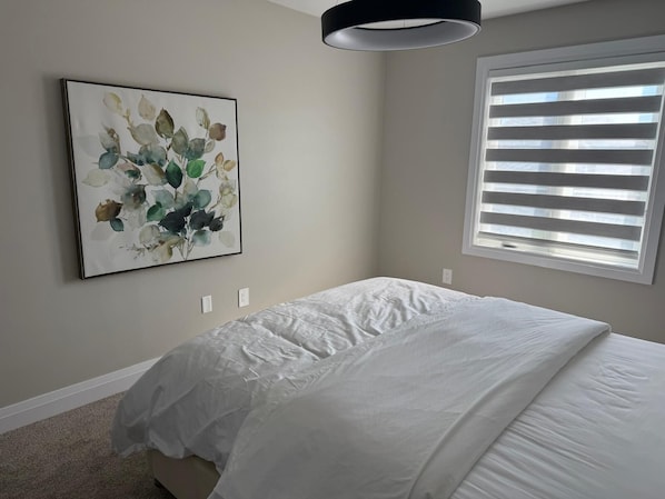 A bedroom with a bed, a window with blinds, and a wall-mounted artwork.