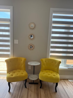 A room with two yellow tufted chairs, a small round table, and three wall-mounted mirrors.