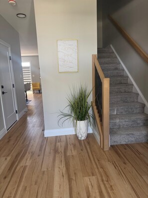 A hallway with wooden flooring, a potted plant, a framed inspirational quote, and a staircase with a wooden handrail. - 5 Bedrooms deluxe, Hyde Park Mall and Western University area Sleep up to 10 (London)