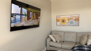 A living room with a flat-screen TV mounted on the wall, a grey sofa with patterned cushions, and a decorative sunburst artwork. - 5 Bedrooms deluxe, Hyde Park Mall and Western University area Sleep up to 10 (London)