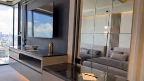 Habitación de hotel moderna con un ventanal grande, un televisor de pantalla plana, un sofá y un espejo que refleja la habitación.
